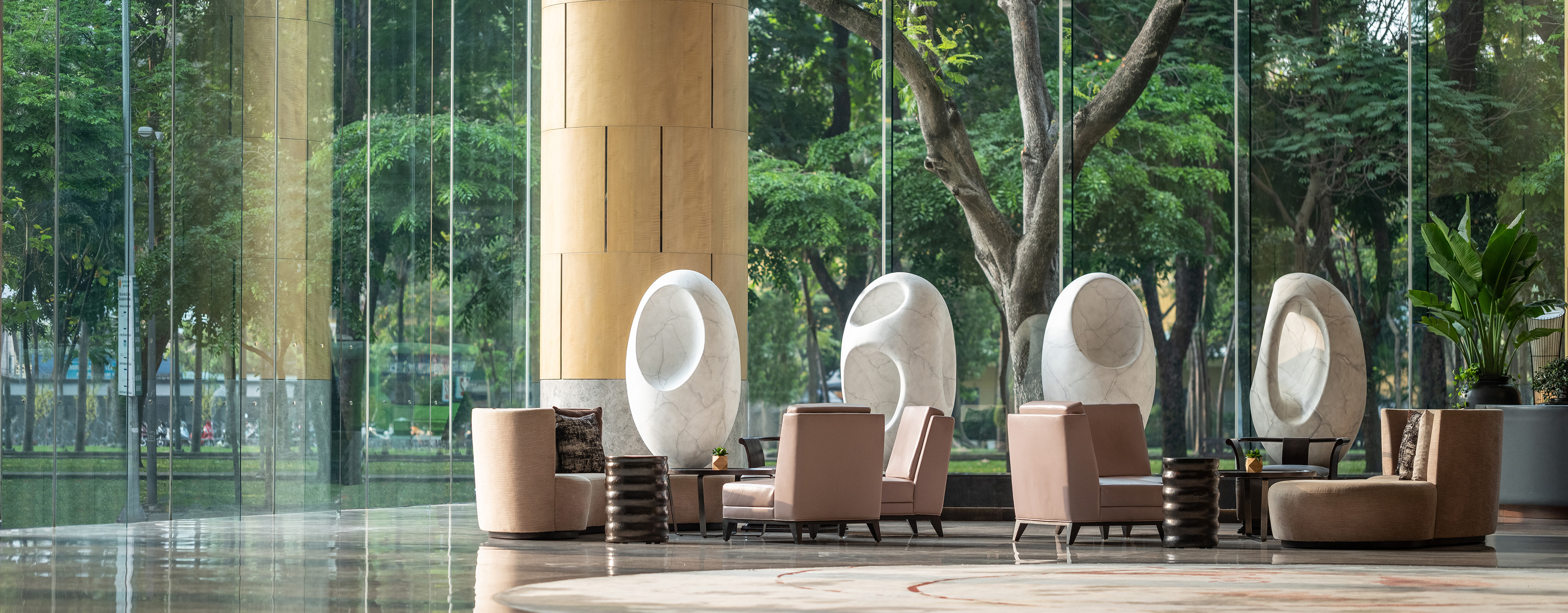 interior of the lounge area in the New World Saigon Hotel showing chairs and oval architecture in front of a large glass wall showing views of trees in the surrounding park
