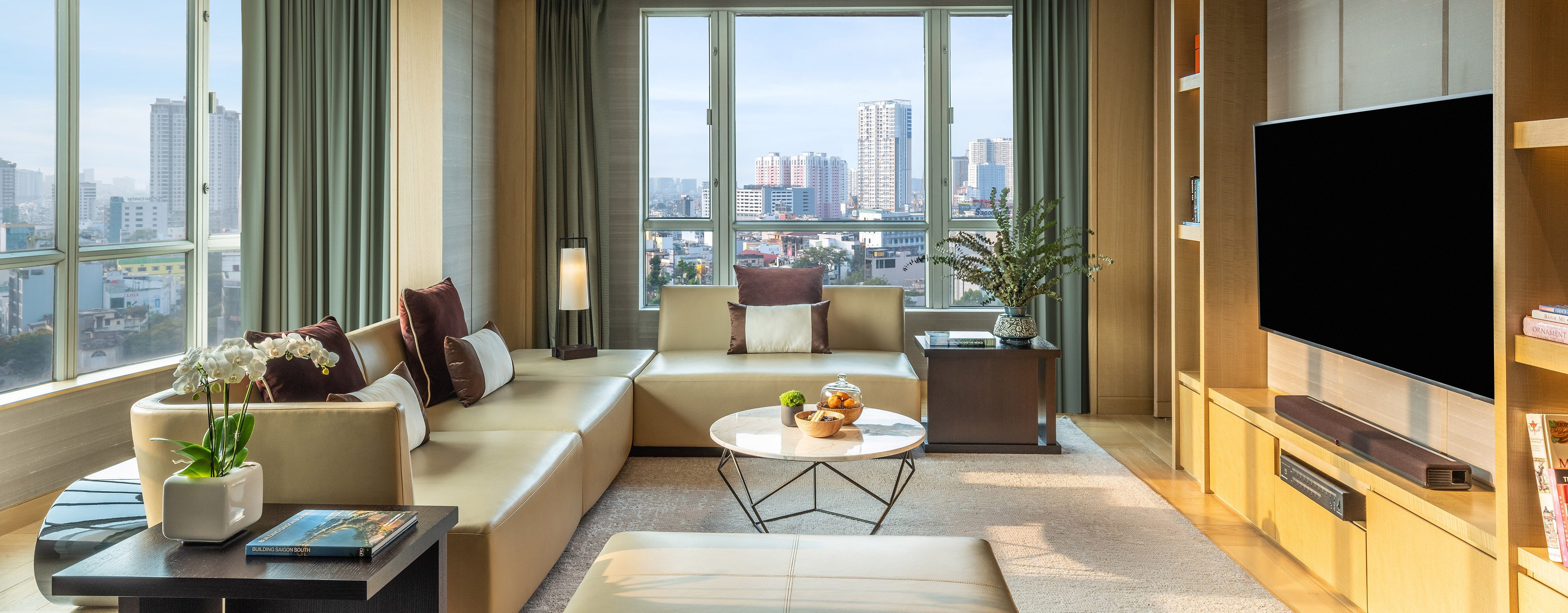 interior of the Presidential Suite living room at the New World Saigon hotel showing comfortable couches across from an entertainment center set in front of large windows with views of Ho Chi Minh City
