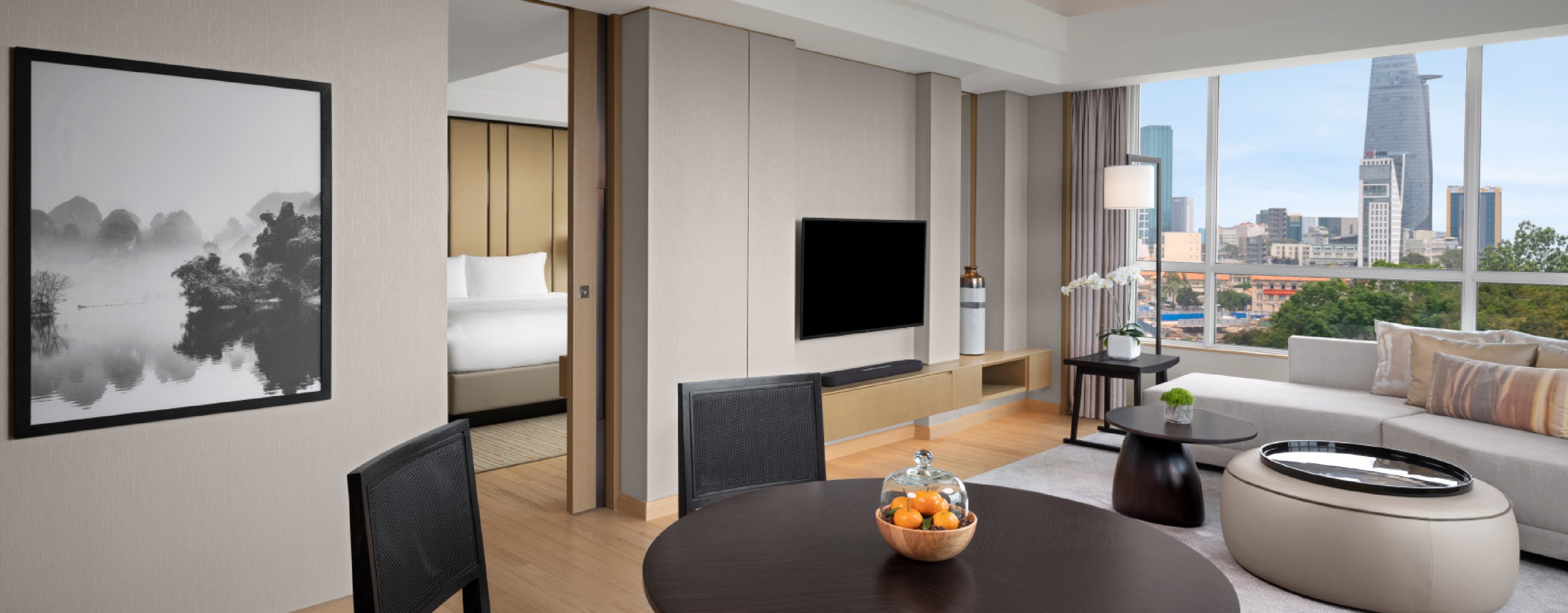 interior of the Executive Suite at a Luxury hotel in Ho Chi Minh City showing an open living room with a dark circular table, a large couch, wall mounted TV and entrance to the bedroom at the New World Saigon Hotel